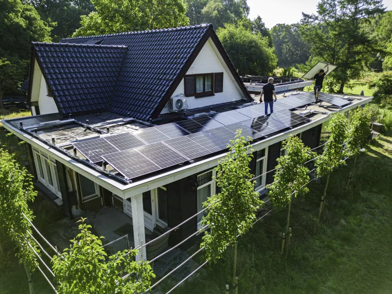 Twee monteurs van Energie Plus leggen zonnepanelen op het platte dak van een woning