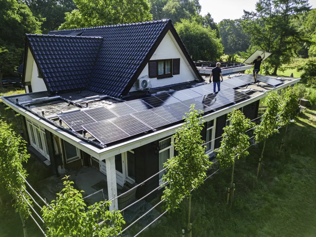 Twee monteurs van Energie Plus leggen zonnepanelen op het platte dak van een woning