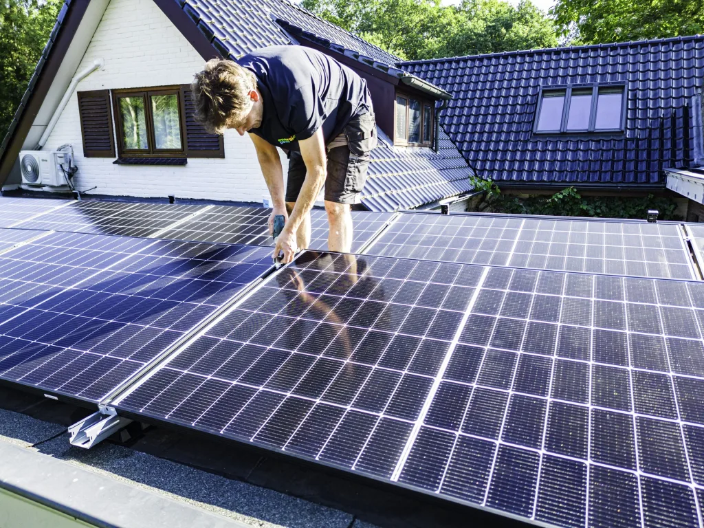 Monteur van Energie Plus schroeft een zonnepaneel vast op een plat dak