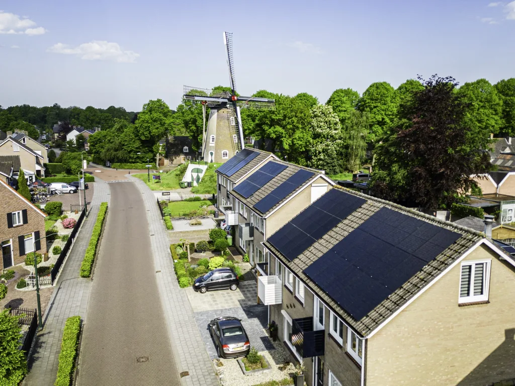 Luchtfoto van een dorpsstraat met zonnepanelen op de daken en een molen op de achtergrond